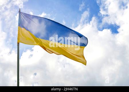 Bandiera dell'Ucraina di fronte al cielo nuvoloso e soleggiato blu Foto Stock