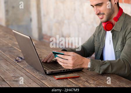 Uomo che effettua acquisti con la sua carta di credito utilizzando il suo computer portatile da una terrazza Foto Stock