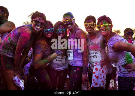 Gruppo di amici che indossano cool Ray-Bans e coperto di polvere colorata posa e sorriso per una foto al Color Walk a Dubai, Emirati Arabi Uniti. Foto Stock