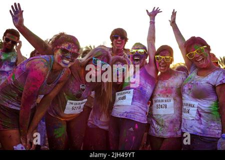 Gruppo di amici che indossano Ray-Bans e coperti di polvere colorata si riuniscono eccitatamente per una foto al Color Walk di Dubai, Emirati Arabi Uniti. Foto Stock