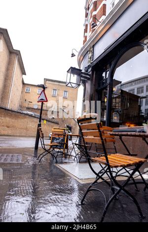 La vista di un'area salotto all'esterno di un cafe' con la pioggia che si riversa giù. I posti a sedere sono vuoti perché nessun cliente vuole bagnarsi. Foto Stock