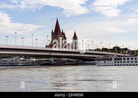 VIENNA, AUSTRIA - 17 agosto 2019: Chiesa di San Francesco d'Assisi, ponte imperiale e fiume Danubio con navi da crociera al porto di Vienna, Austria Foto Stock