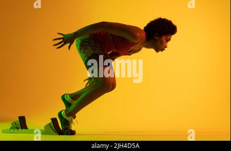 Immagine di atleta afro-americana che si prepara per correre in luce gialla Foto Stock