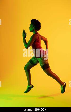 Immagine verticale di atleta afro-americana che corre in luce gialla Foto Stock