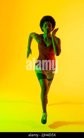 Immagine verticale di atleta afro-americana che corre in luce gialla Foto Stock