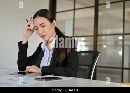 Una giovane e seria imprenditrice asiatica o una lavoratrice finanziaria femminile si è concentrata sul suo progetto finanziario, esaminando e analizzando i dati finanziari. Foto Stock