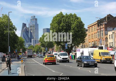 Guarda verso ovest verso la città di Londra lungo Mile End Road accanto alla stazione Whitechapel. Mostra il traffico occupato, la pista ciclabile e le torri cittadine oltre. Foto Stock