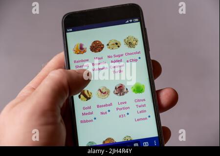 L'uomo ordina cibo per telefono. La mano maschile seleziona un gelato dal menu. Baskin-Robbins è una catena di ristoranti americani specializzati in gelati e pas Foto Stock