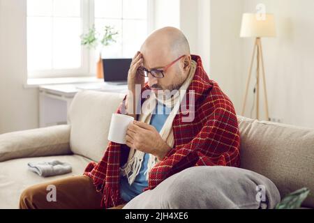L'uomo malato infelice a casa cura l'influenza e il raffreddore con una bevanda medicinale dal gusto sgradevole. Foto Stock