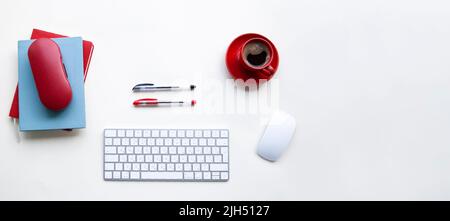 Tastiera e mouse bianchi con penne rosse e nere, tazza di caffè, notebook su tavolo bianco Foto Stock