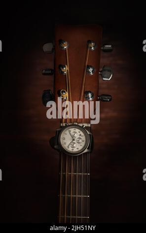 Orologio da polso argento sul collo della tastiera della chitarra acustica, girato in studio con sfondo di legno scuro Foto Stock