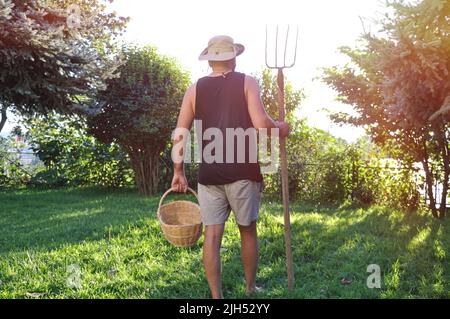 Un giovane agricoltore cammina attraverso il suo campo con una forchetta. Il concetto di raccolta. Estate e autunno in azienda sono pieni di temi biologici Foto Stock