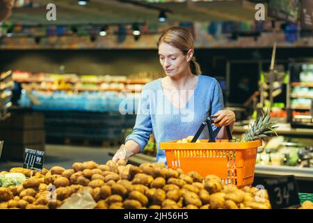 Una casalinga donna in un supermercato sceglie le verdure nel reparto di alimento, una donna mette le patate in un cestino di shopping Foto Stock