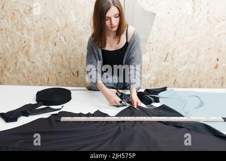 Giovane donna che taglia il tessuto nero in officina Foto Stock