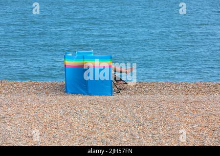 Una coppia si rilassa su una spiaggia di ghiaia con un frangivento Foto Stock