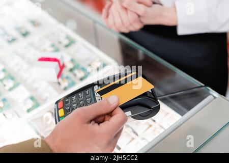 Vista ritagliata dell'uomo che paga con la carta di credito vicino al venditore sfocato in negozio di gioielli Foto Stock