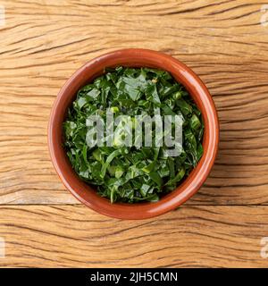 Strisce di kale cotte, tipico fiancata brasiliana feijoada in una ciotola su tavola di legno. Foto Stock