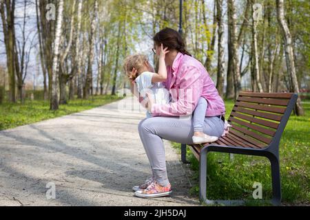 Una madre cullerà la figlia su e giù mentre si siede su una panchina in un parco cittadino. Foto Stock