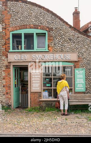 Cley accanto al mare Smokehouse, vista di una donna visitatore di Cley accanto al mare guardando nella finestra del Cley Smokehouse, costa nord norfolk, Inghilterra Foto Stock