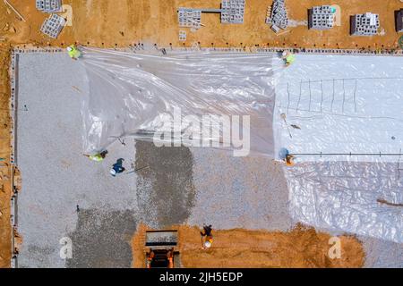 Lavorare sul livellamento della ghiaia in cantiere con un escavatore prima di preparare il versamento del calcestruzzo sulla fondazione dell'edificio Foto Stock