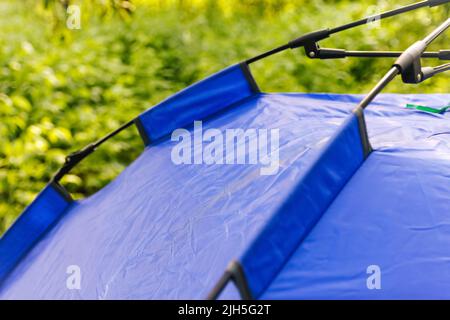 Defocus autumatico closeup tenda turistica blu in piedi su sfondo verde natura. All'aperto. Concetto di turismo. Vacanze estive nella foresta, campeggio. Cacciatore Foto Stock