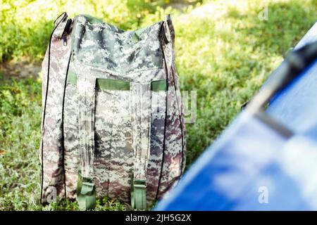 Sfocatura blu tenda turistica aperta in piedi su sfondo verde natura. Zaino militare. Concetto di turismo. Vacanze estive nella foresta, campeggio. Sfocato. Hunte Foto Stock