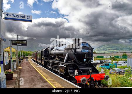 TRENO A VAPORE JACOBITE DI FORT WILLIAM SCOTLAND PASSANDO ATTRAVERSO LA STAZIONE DI BANAVIE CON BEN NEVIS SULLO SFONDO Foto Stock