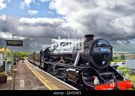 FORT WILLIAM SCOZIA IL TRENO A VAPORE JACOBITE PASSA ATTRAVERSO LA STAZIONE DI BANAVIE CON BEN NEVIS SULLO SFONDO Foto Stock