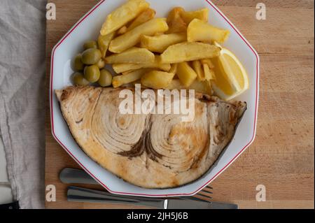 Piatto di pesce, bistecca alla griglia di pesce spada o spada servita con patate fritte francesi e olive verdi, da vicino Foto Stock