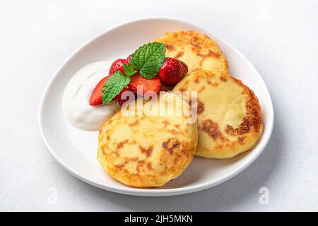 Pancake al formaggio casolare con panna acida e bacche su sfondo chiaro. Foto Stock