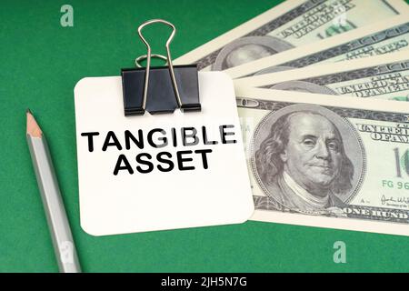 Concetto aziendale. Su una superficie verde, una penna, dollari e in una clip paper con l'iscrizione - asset tangibile Foto Stock