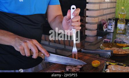 Uomo che taglia carne al barbecue con coltello e forchetta con denti, Brasile, Sudamerica, accessori di carne e condimenti, Brasile, Sudamerica Foto Stock