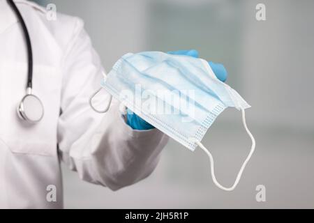 primo piano della mano del medico con una maschera medica per il viso per la protezione contro le infezioni Foto Stock