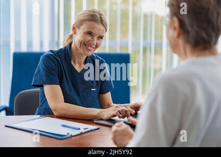 Il terapeuta sorridente conduce un esame preventivo di una donna nel suo ufficio in una clinica moderna Foto Stock