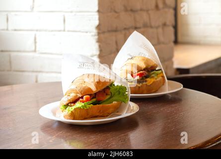 Due panini con croissant con salmone, formaggio spalmabile e insalata verde in confezione di carta su un tavolo di legno da caffe'. Colazione da asporto Foto Stock