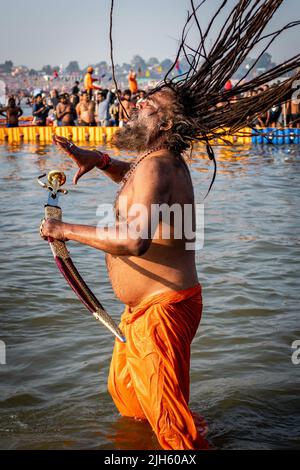 Un uomo indù con lunghi doadlock e con una spada bagna al Triveni Sangam al Kumbh Mela Festival ad Allahabad (Prayagraj), India. Foto Stock