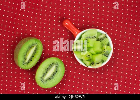 Due metà di kiwi. Kiwi tagliato a pezzi in un piatto rosso. Sfondo rosso puntino polka Foto Stock