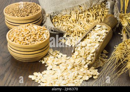 Grani di avena nel sacchetto. Avena macinata in un cucchiaio di legno. Orzo di ramoscello. Grano saraceno e grano in scatole di legno Foto Stock