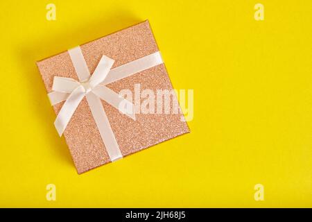 Scatola regalo beige è legato con nastro con arco su sfondo giallo Foto Stock