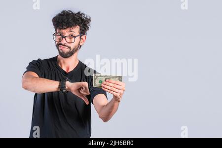 Triste persona che tiene una banconota con il pollice giù, uomo triste con una fattura del dollaro, concetto di uomo con i problemi di soldi Foto Stock