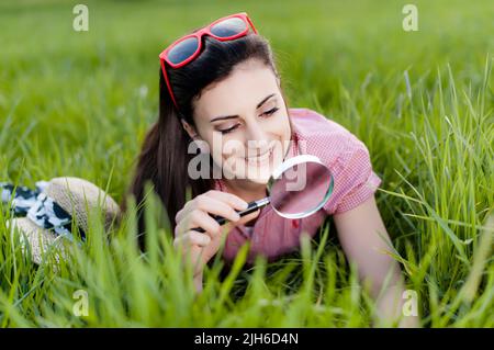 Giovane donna sdraiata in prato con lente d'ingrandimento Foto Stock