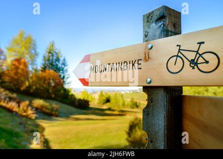 Un cartello stradale in legno che mostra una bicicletta e un sentiero di montagna. Una soleggiata giornata autunnale per un tour in bicicletta attraverso la natura. Foto Stock