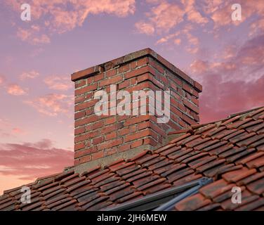 Primo piano di camino in mattoni rossi contro un cielo colorato tramonto per gas di combustione e isolamento domestico su tetto piastrellato. Design architettonico in casa Foto Stock