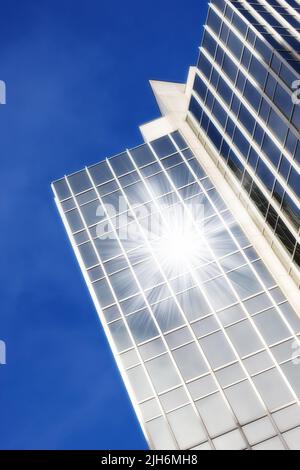 Finestre geometriche in vetro su un grattacielo con il sole che riflette una lente svasata su uno sfondo blu cielo dal basso. Dettagli architettonici esterni di a. Foto Stock