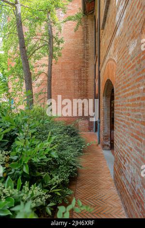 Il percorso in mattoni rossi a forma di spina di pesce alla base di un edificio in Itally conduce oltre arbusti e all'ingresso principale dell'edificio Foto Stock