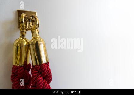 Primo piano di nobile bordeaux rosso nobile lucchetto corda catena corda con le estremità dorate agganciate su un gancio contro sfondo bianco parete con spazio copia come Foto Stock