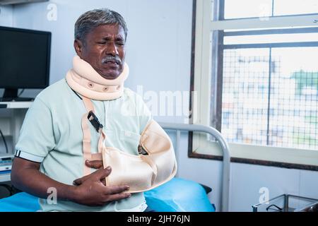 Uomo anziano che soffre di lesioni di frattura del collo e della mano mentre si siede sul letto dell'ospedale - concetto di medicare, trattamento sanitario e sicurezza. Foto Stock