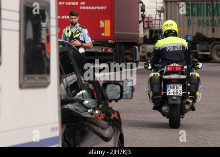 Ratingen, Germania. 16th luglio 2022. Un motociclista della polizia dirige un'auto con una roulotte fuori dall'autobahn del A3 vicino Ratingen all'area di servizio di Hösel per un controllo. La polizia utilizza il punto intermedio delle vacanze estive come opportunità per controlli sul traffico a livello nazionale. Credit: David Young/dpa/Alamy Live News Foto Stock