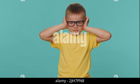 Non vuoi ascoltare e ascoltare. Frustrato infastidito irritato bambini bambino ragazzo coprendo le orecchie e gesturando No, evitando consiglio ignorando rumore sgradevole voci forti. Bambino giovane su sfondo blu parete Foto Stock