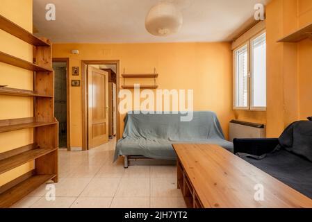 Camera con mobili in legno irregolari, divano letto con tessuti e pareti color giallo crema Foto Stock